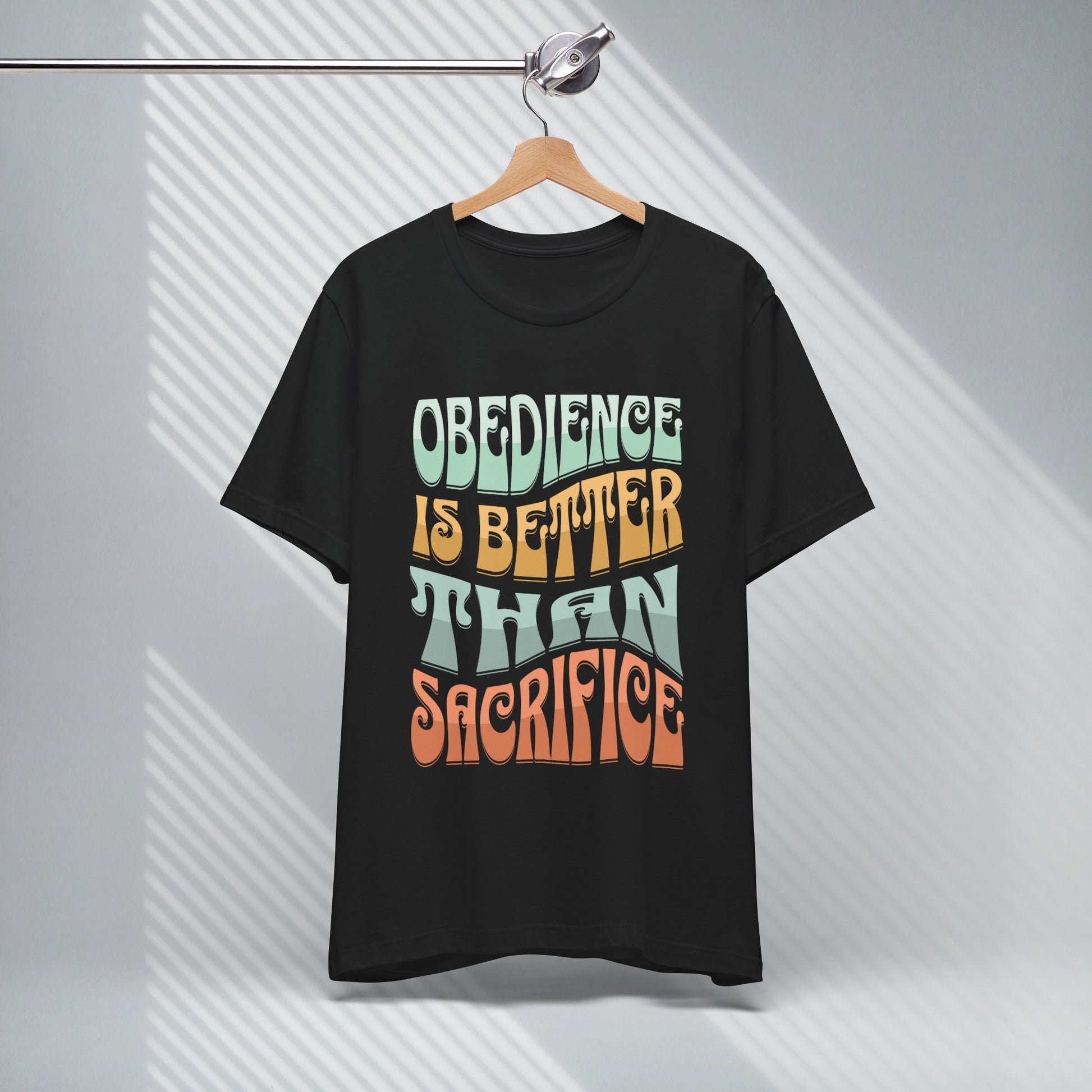 black short sleeve crew neck christian graphic tee hanging on a hanger the shirt says obedience is better than sacrifice