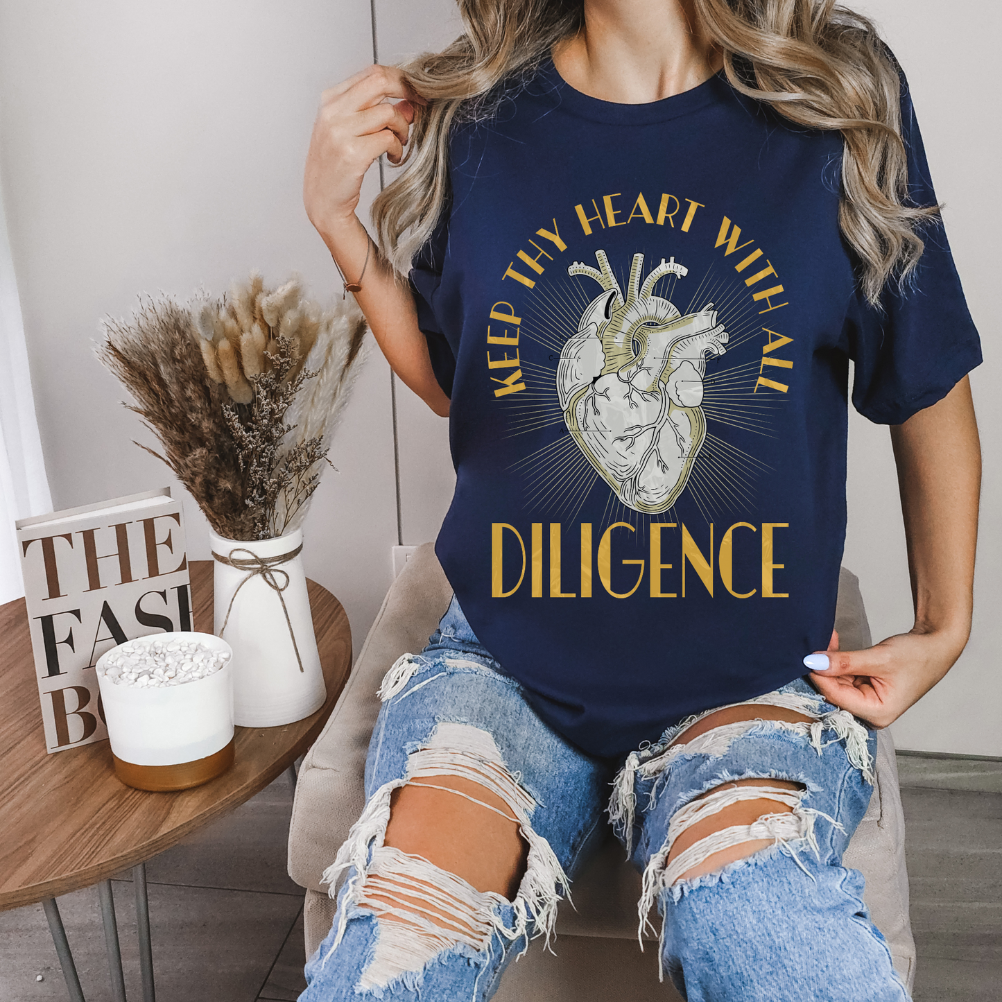 woman sitting in a chair wearing a navy crewneck christian t shirt that says keep thy heart with all diligence bible verse shirt