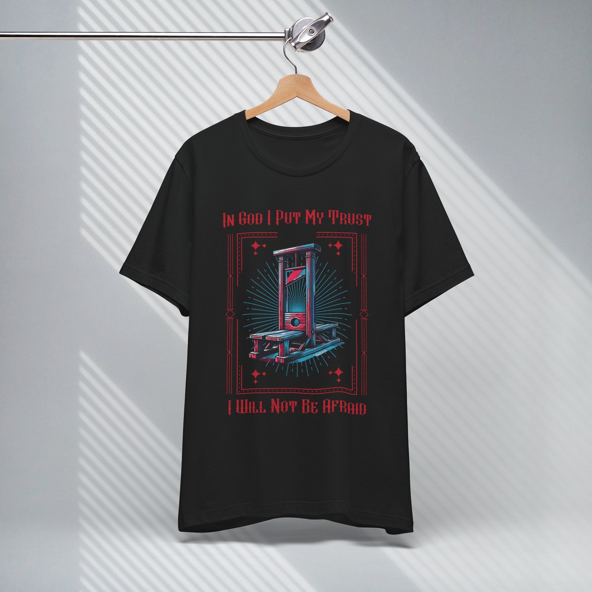 modern christian apparel graphic tshirt on a hanger with image of a guillotine that says in god i put my trust i will not be afraid