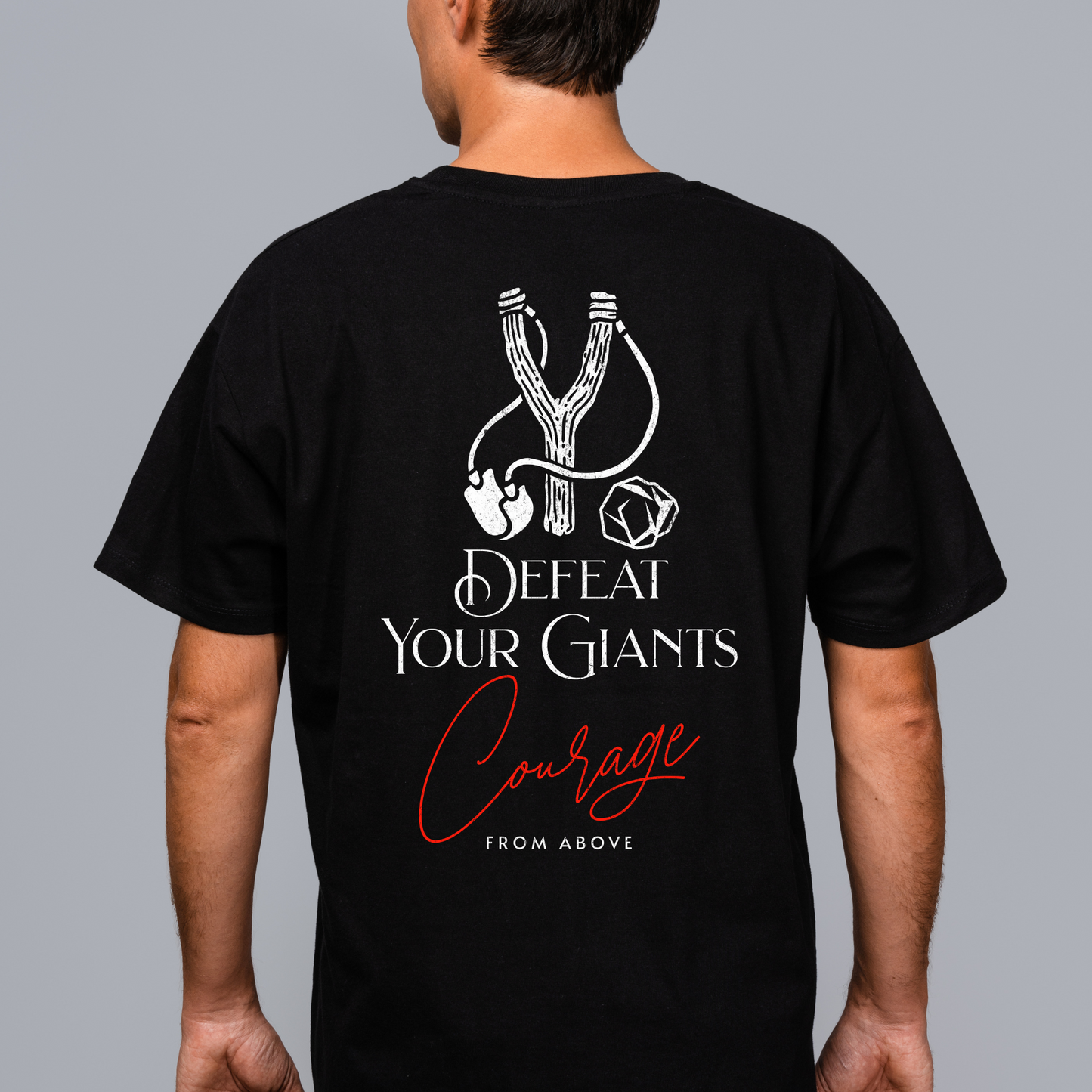 back of a black short sleeve crewneck christian graphic tee with a sling shot and stone and the text defeat your giants